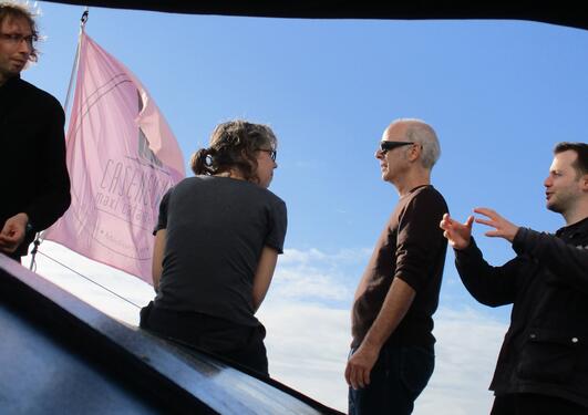 Four people next to each other, with blue skies and a pink flag in the background