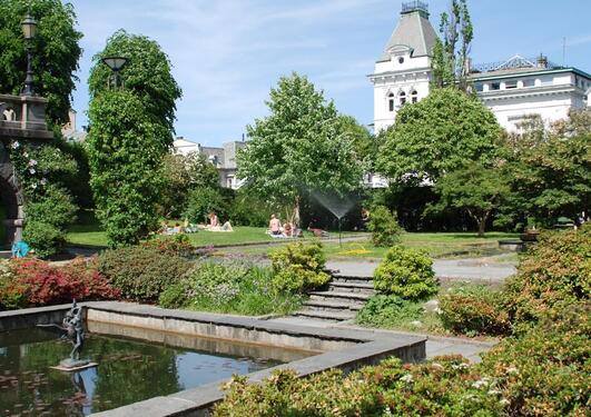 A white house on the background of a blue sky, greenery and a fountain in the front