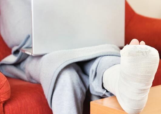 Man with bandaged leg sitting with a laptop.