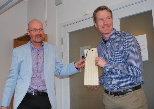 Instituttleder Jan Heiret, t.v., overrekker en vinflaske til Eivind Heldaas Seland, som oppnådde flest publikasjonspoeng av instituttets forskere i 2016.