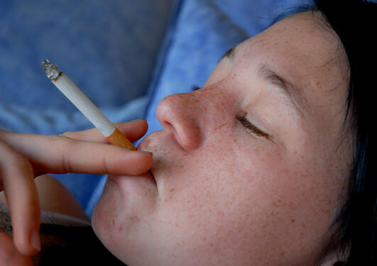 ungdom som røyker - hen ligger på en pute med øynene lukket og har en sigarett mellom fingrene