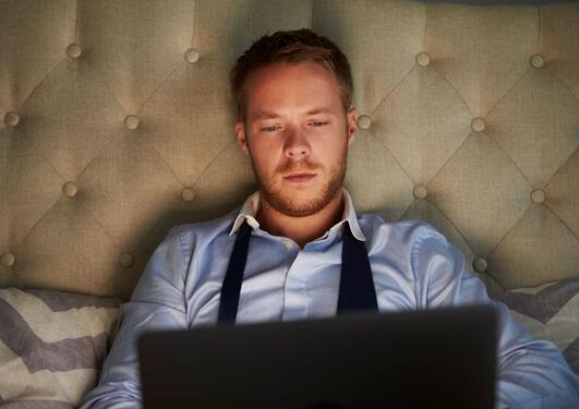 Ung mann sitter i sengen med laptopen på fanget