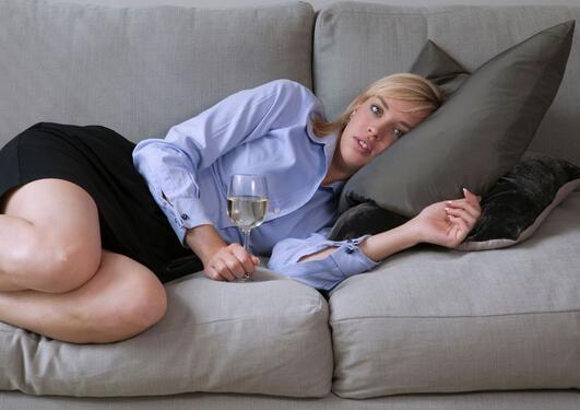 Kvinne ligger på sofaen med et glass hvitvin i hånden