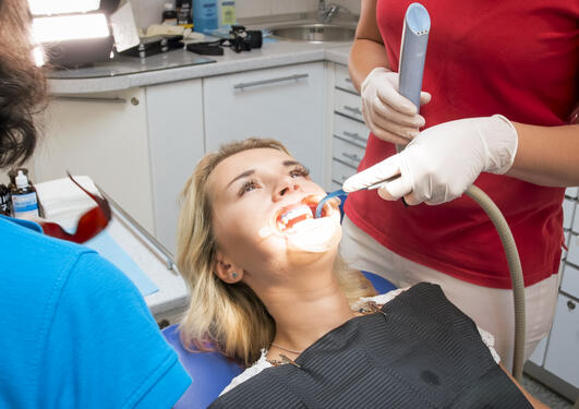 kvinne hos tannlegen i tannlegestolen med munnen åpen. to tannpleiere eller tannleger står over henne