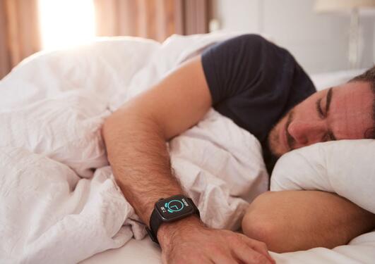 Mann sover i sengen med smartklokke på armen