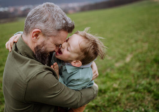 bilde av en mann som holder en gutt som holder på å lekent bite han i nesa 