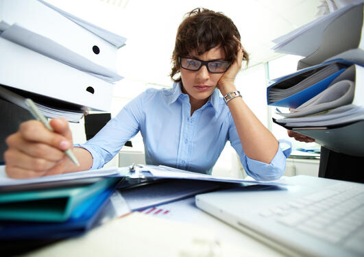 Extremely overworked woman at her desk surrounded by paper work; used to illustrate article about research on work addiction.