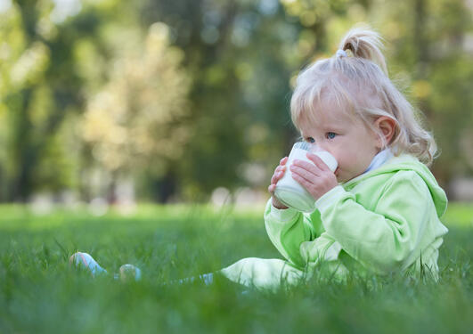 Et lite barn sitter i gresset og drikker et glass melk