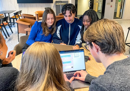 Tre personer sitter ved en Apple Mac og tar en utdanningstest på nettet