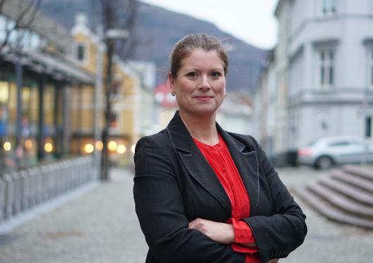 Bilde av Strønen med rød topp og svart blazer foran Bergens-landskap