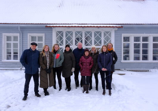 Group photo of the nine meeting participators in front of a light blue, wooden building with a lot of windows. Snow on the ground and on the house roof.