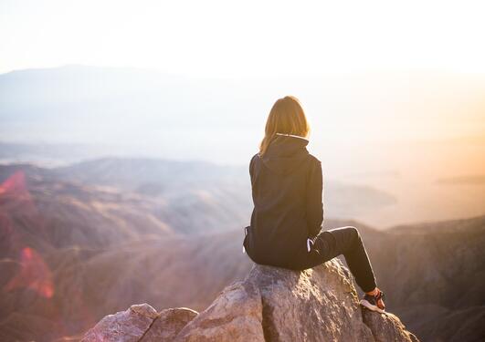 Kvinne sitter på en fjelltopp og ser utover