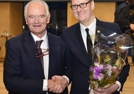two men shaking hands with certificate and flowers