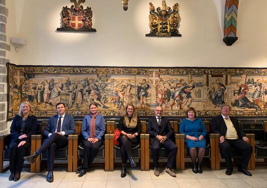 The image portrays professor Sören Koch together with his international colleagues. Everyone is sitting in a chair beneath classic Hanseatic coat of arms and art.
