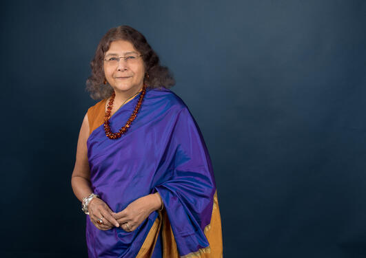 A women with brown hair, a purple and orange sari and a read necklace