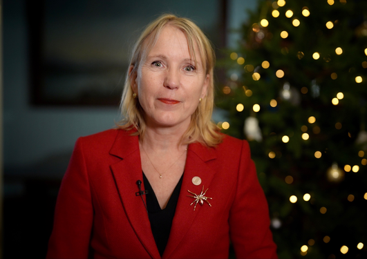 Rektor Margareth Hagen foran juletre med julelys i rød jakke
