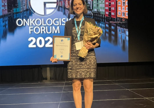 Katrin Kleinmanns smilende på scenen med blomster og diplom.