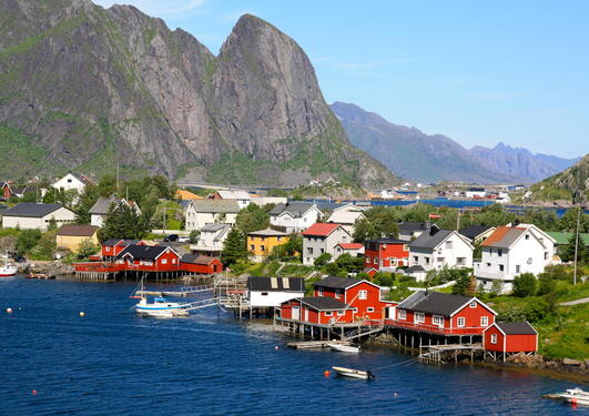 A small and colourful village by the sea, tall mountains and blue skies in the background