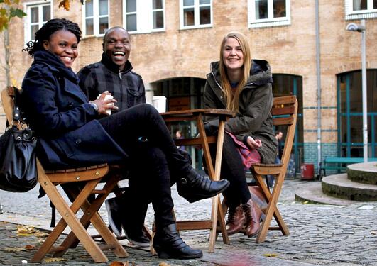 Two female and one male student sitting around a table outside on campus drinking coffee