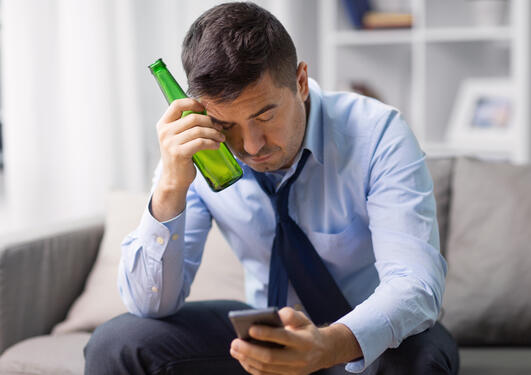 Bilde viser mann med flaske som scroller på mobil