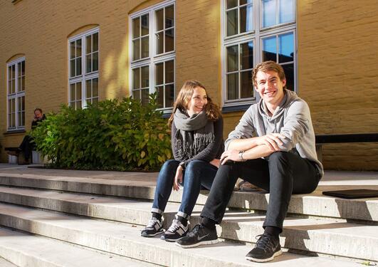 Jente og gitt sitter i solen på trappen på Sydneshaugen skole  