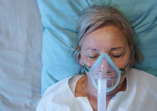 Eldre kvinne ligger på sykeseng med oksygenmaske på 