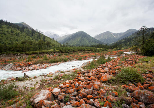 Landscape view looking upriver towards mountains in Sichuan, China, with large rounded boulders on the side of the river covered in red lichens