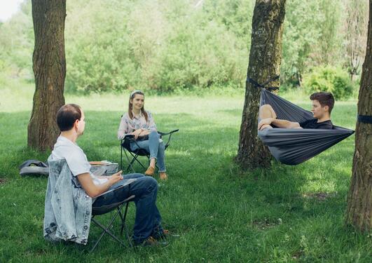 Three people sitting socially distanced among trees. Two of them in lawn chairs and the last in a hammock.