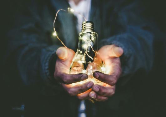 En person holder en lysende glødepære i hendene