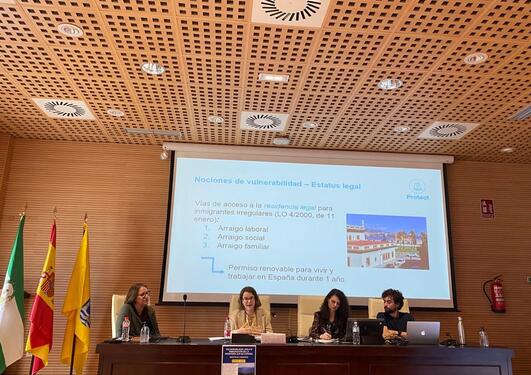 Four people presenting at a seminar in front of a screen with a PowerPoint presentation showing