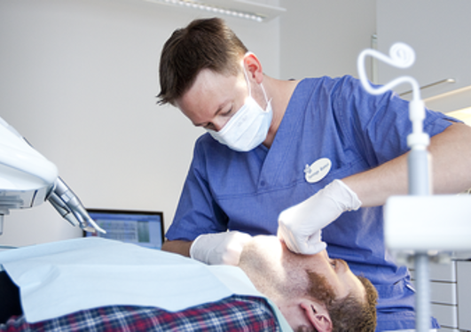 Tannlege ser in i munn til pasient på legekontor