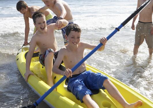 Tenåringsgutter leker i vannkanten med en gul kajakk 