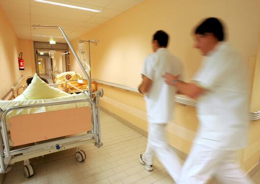 Bilde fra et sykehus hvor to ansatte haster forbi to sengeliggende korridorpasienter