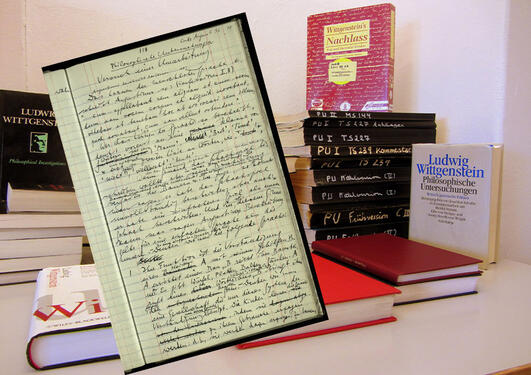 Bilde av Wittgensteins Nachlass sammen med en rekke av Wittgensteins publikasjoner og med utdrag fra håndskrevet manus som bildet i forkant.